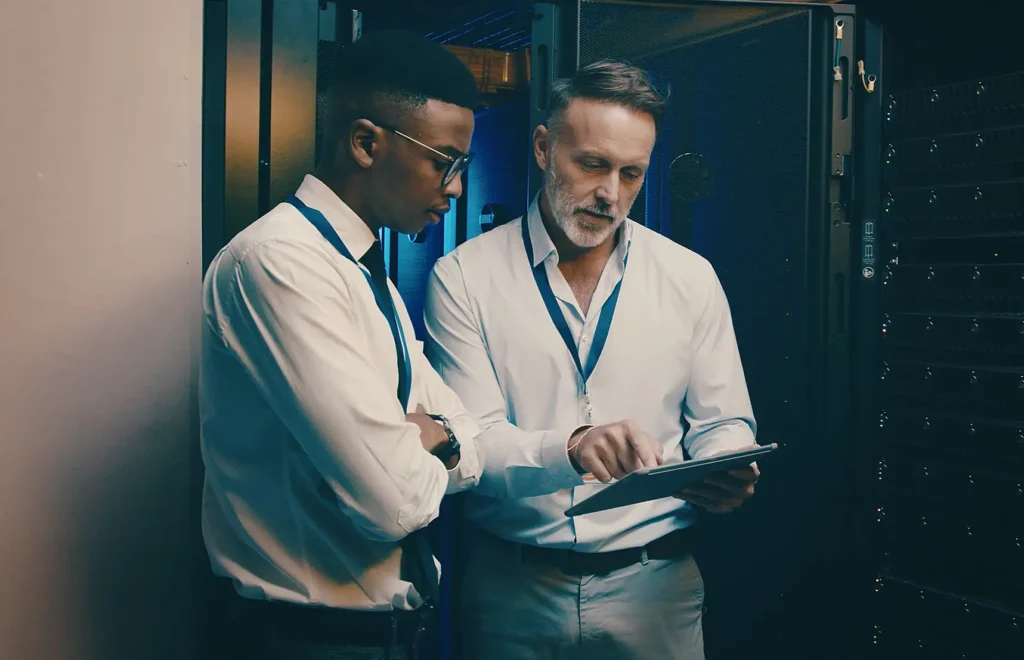 Men, tablet and talk in server room with inspection, review and system maintenance report