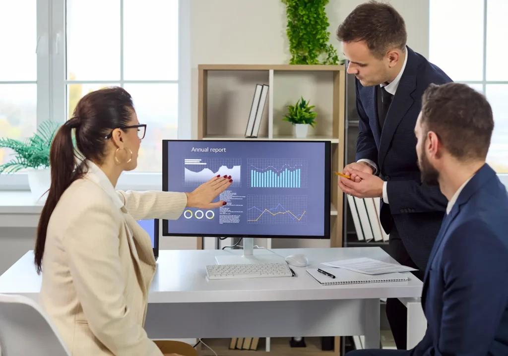 Business meeting as analyst discusses finance charts. A monitor shows data analytics