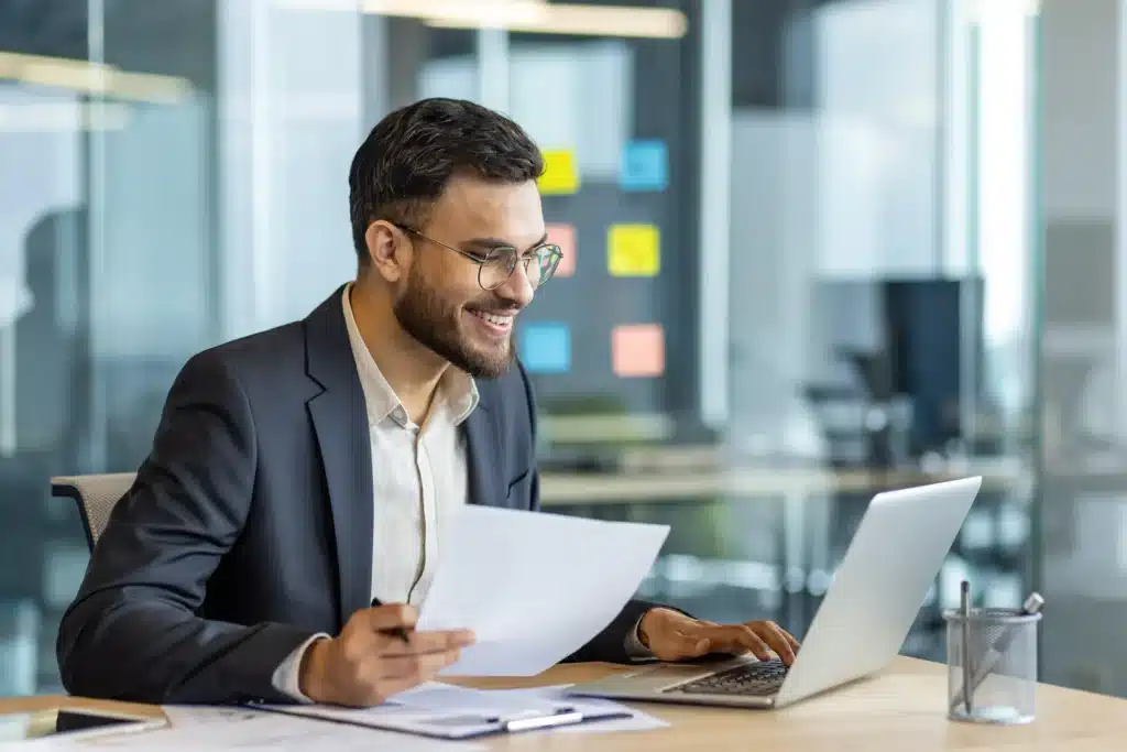 Latin American businessman in a formal suit smiling while working on a laptop